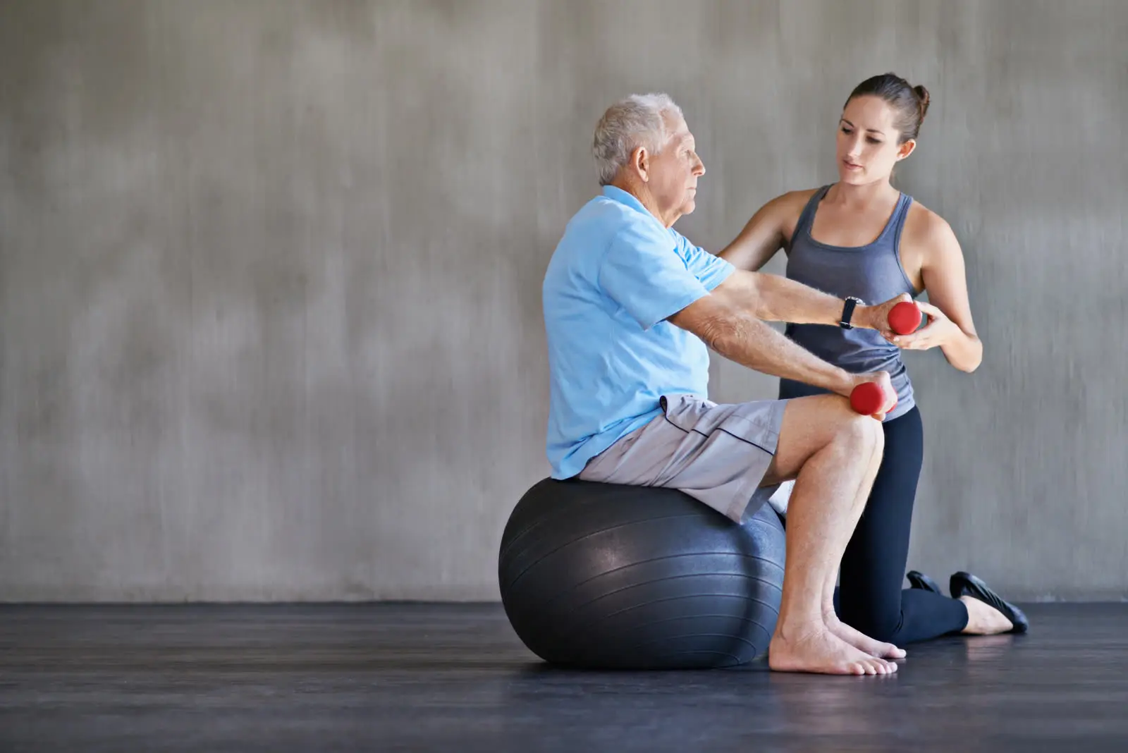 Physiotherapeutin übt mit einem Senior auf dem Gymnastikball